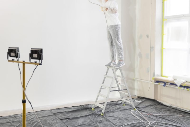 worker-painting-wall-ladder-full-shot
